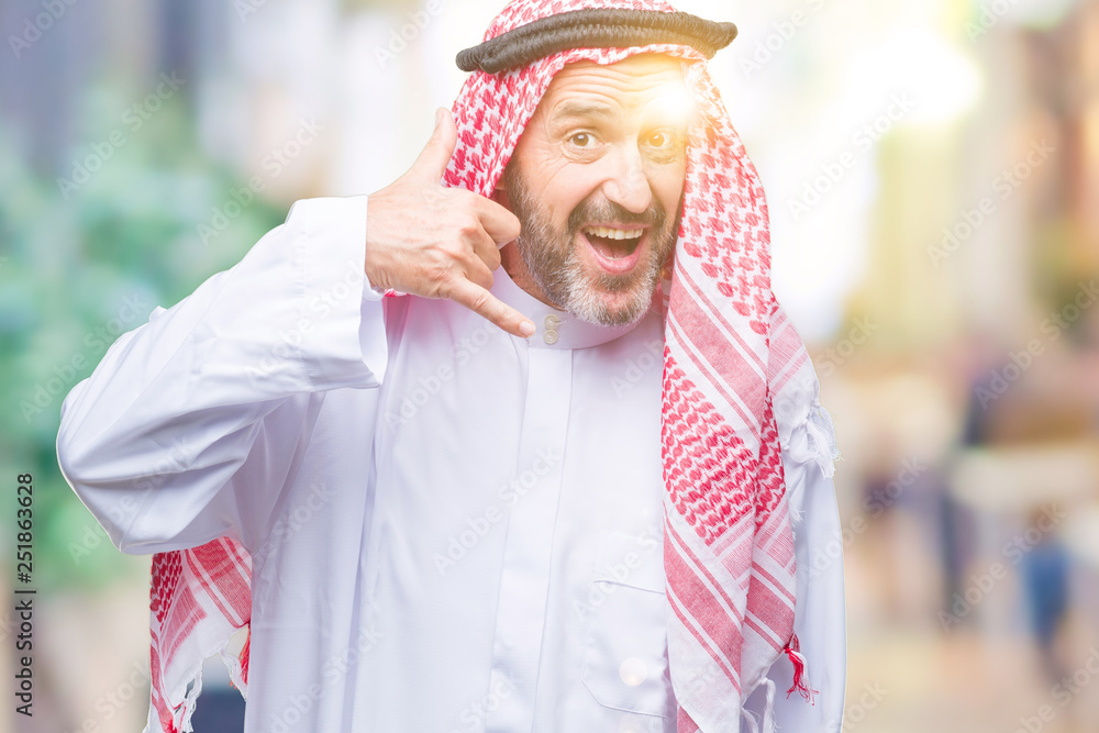 Senior arab man wearing keffiyeh over isolated background smiling doing phone gesture with hand and fingers like talking on the telephone. Communicating concepts.