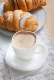 Cappuccino with croissants. Cup of coffee with milk and two croissants  stands on a table.