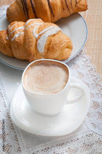 Fototapeta Naklejka Na Ścianę i Meble -  Cappuccino with croissants. Cup of coffee with milk and two croissants  stands on a table.