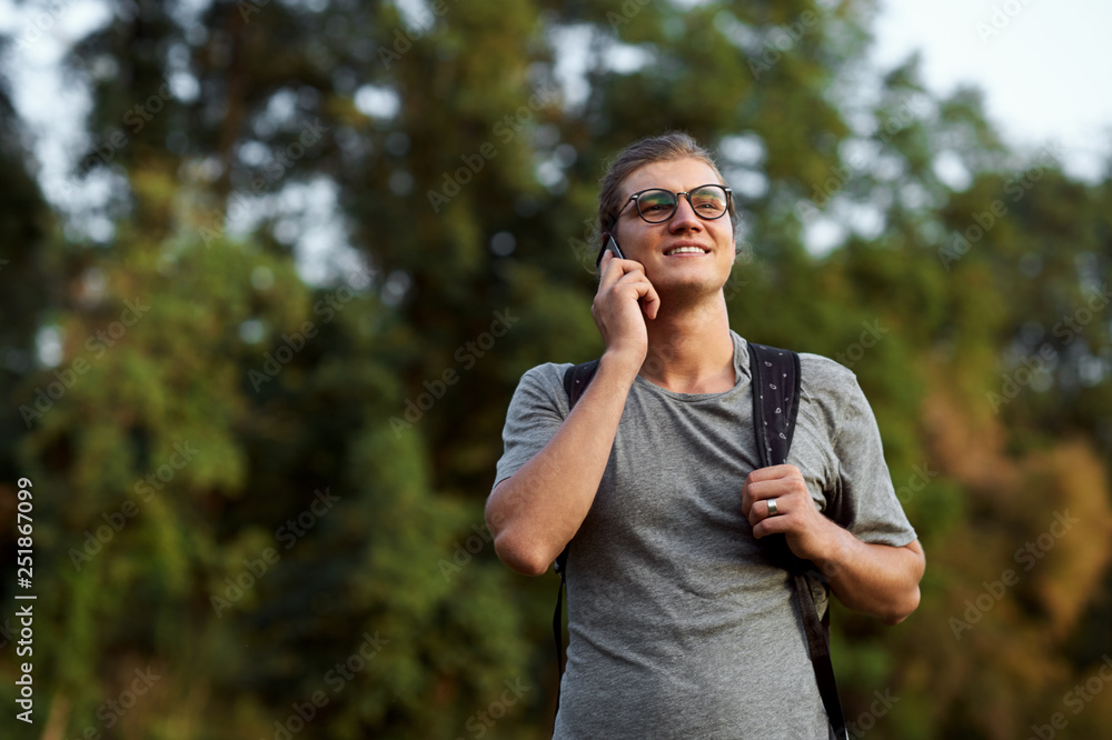 Young caucasian student with backpack, wearing casual clothes and using smartphone outdoor in the public park. Young caucasian student with backpack, wearing casual clothes and using smartphone outdoor in the public park.