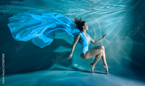 Fotografie Girl portrait posing underwater in blue fashion dress in swimming pool alone in
