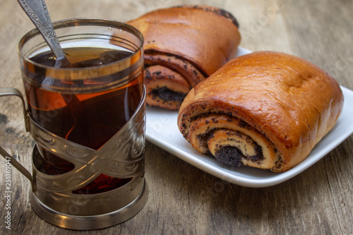 Fresh bread rolls with poppy seeds, tea and pastry on a wooden table