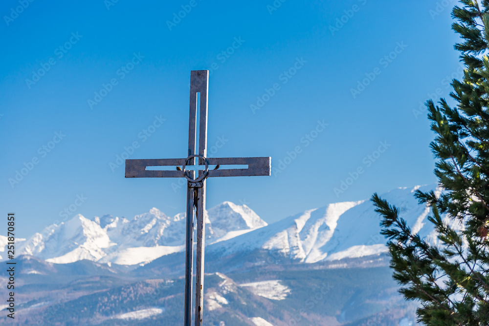 A metal cross visible in the foreground in the background a beautiful view of the Polish Tatra Mountains. Sunny, beautiful day in the winter, snow-capped mountains and blue sky. A metal cross visible in the foreground in the background a beautiful view of the Polish Tatra Mountains. Sunny, beautiful day in the winter, snow-capped mountains and blue sky.