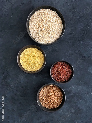 Red rice, buckwheat, millet and oatmeal on dark background