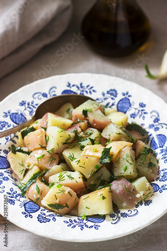 Traditional cold potato salad with onions and herbs on a linen tablecloth background. Rustic style.