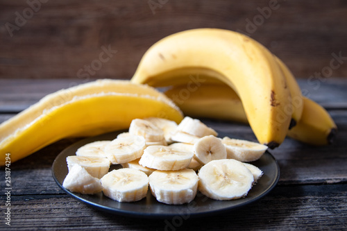 Bunch of bananas, sliced banana on black plate and peel, on old wooden table