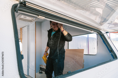 Valokuva Young smiling man with a drill restoring his old caravan