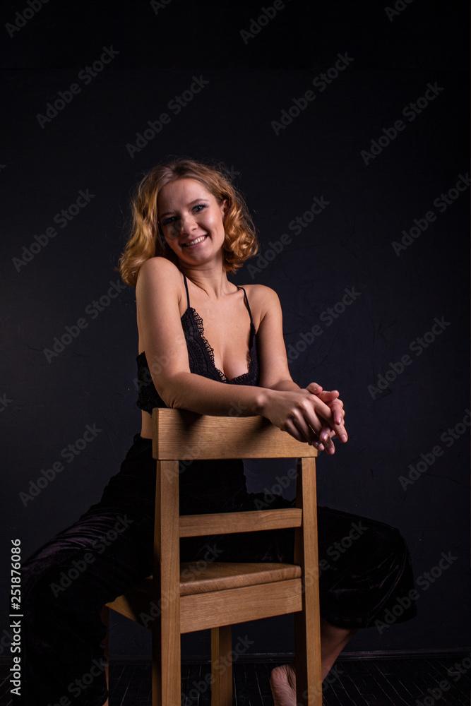 Fototapeta premium A pretty woman with a good figure is standing in a bra and black pants near the bar stool in the room.