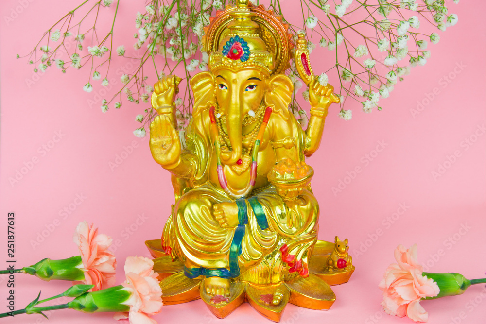 Lord Ganesha and flowers statuette on a vibrant pink background