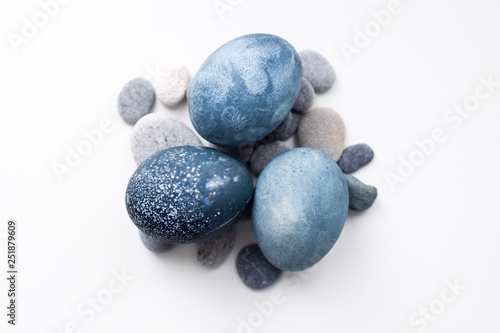 Three colored blue, gray marble eggs lie on the stones on a white background