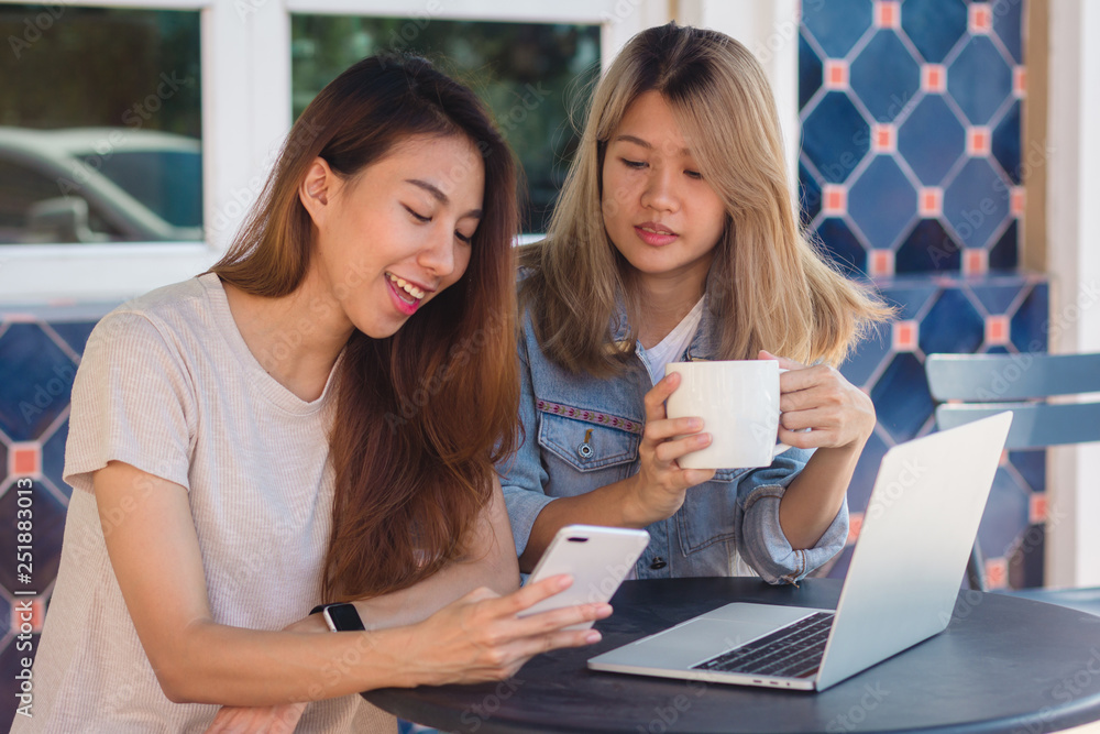 Asian young women working on laptop using and looking smartphone and drinking coffee while sitting in cafe. Lifestyle women communication and working in coffee shop concept. Asian young women working on laptop using and looking smartphone and drinking coffee while sitting in cafe. Lifestyle women communication and working in coffee shop concept.