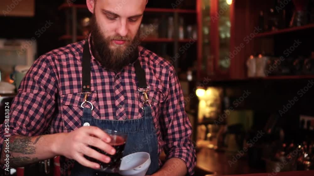 Experienced male barista with tattoos and beard busy making alcohol cocktail on bar counter in slow motion Experienced male barista with tattoos and beard busy making alcohol cocktail on bar counter in slow motion