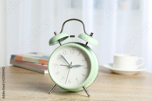 Beautiful retro alarm clock with cup of coffee, succulent plant and books on table against light background