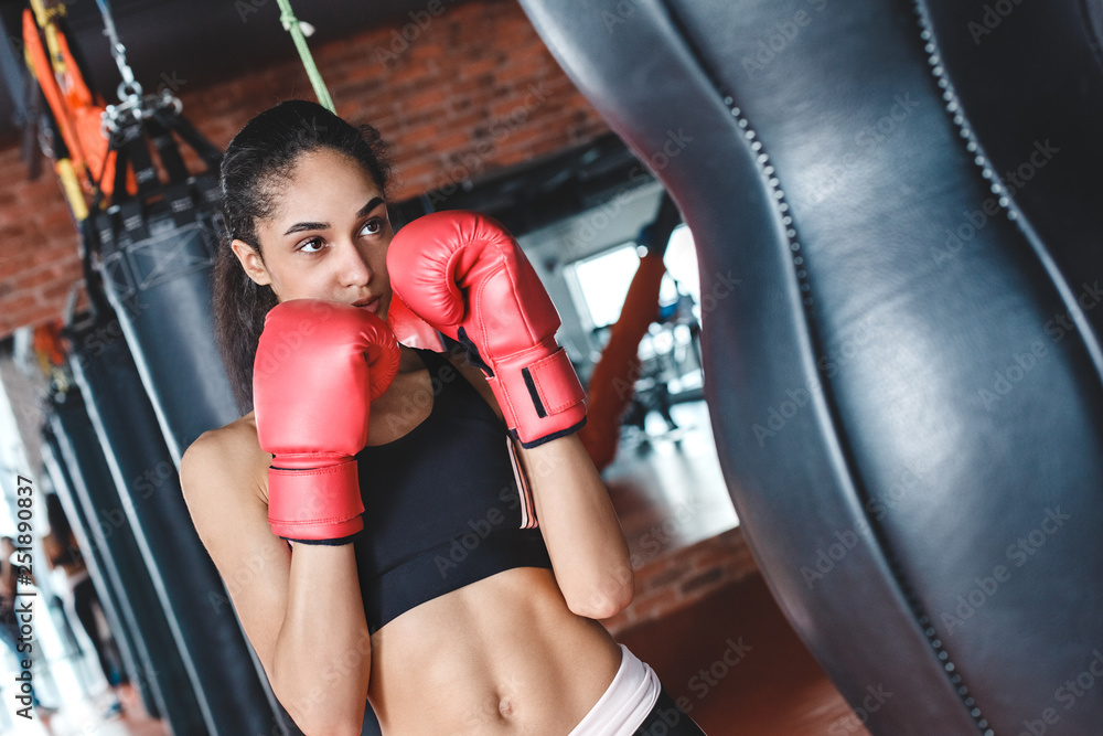 Young woman in boxing gloves in gym standing ready to kick punching bag excited