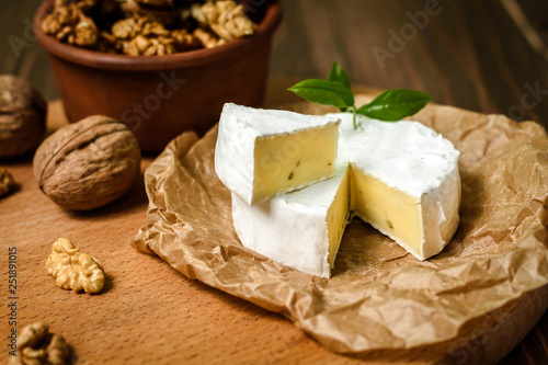 Camembert or Brie cheese with walnut kernels on wooden wooden background. Copy space. white mold grows on top Penicillium camemberti. 