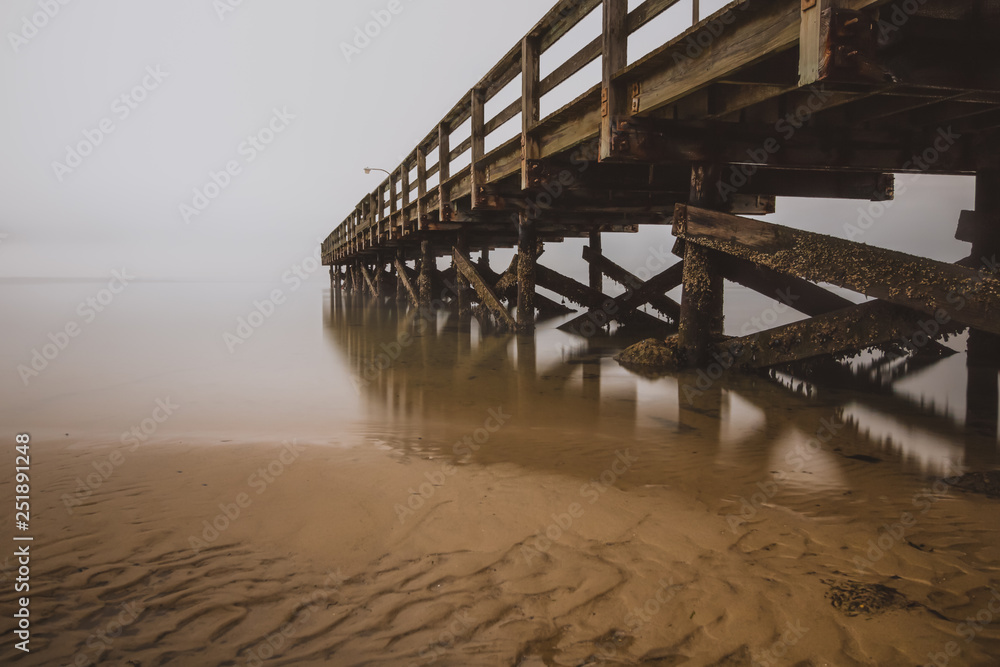 Fishing pier disappearing into the sea in foggy conditions. Dramatic seascape, creepy moody scene. 