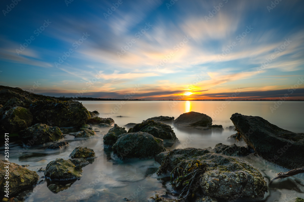 The sun setting on the horizon along a rugged coastline. Green algae on rocks as the tide recedes. 