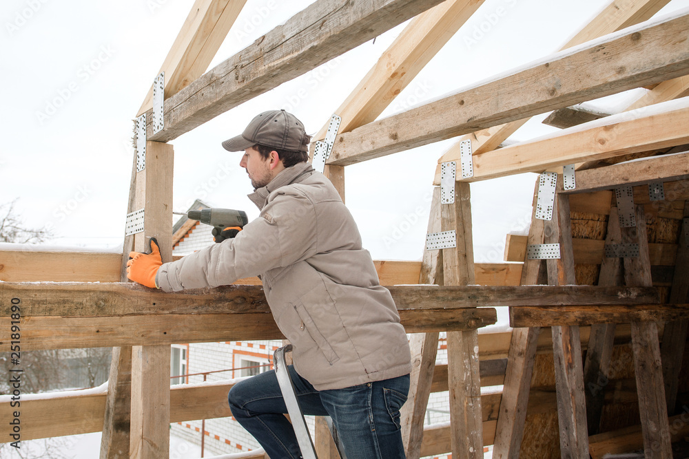 Carpenter using electric screwdriver. Man builds a roof of wooden planks. Attic renovation. Building construction outdoor. Countryside house. Farm householding. Carpenter using electric screwdriver. Man builds a roof of wooden planks. Attic renovation. Building construction outdoor. Countryside house. Farm householding.