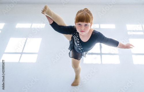 Fototapeta Naklejka Na Ścianę i Meble -  Little girl performs a gymnastic twine in the studio on a white background. The concept of fitness and sport and a healthy lifestyle