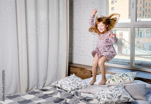 Happy little girl jumping on bed. Happy and carefree childhood