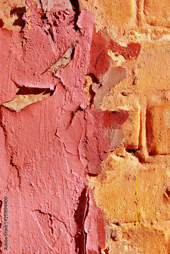 Cracked soft pink paint, plaster surface on yellow brick wall, grunge vertical shabby background detail close up