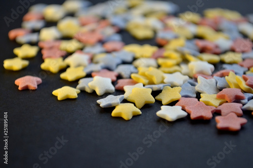 A lot of sugar colored stars on black background macro, background for confectioners with copyspace