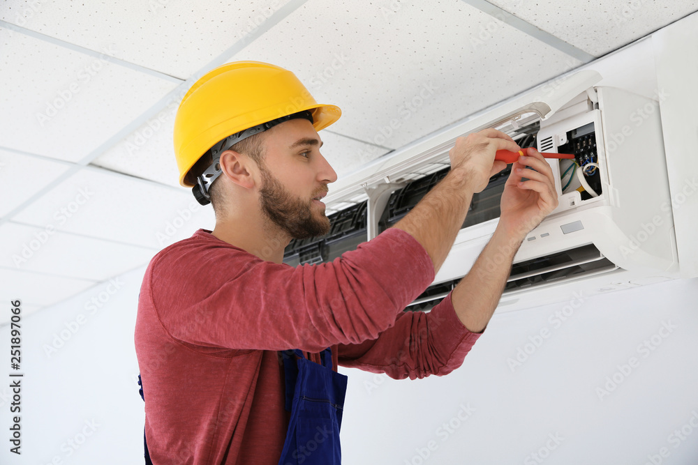 Electrician with screwdriver repairing air conditioner indoors Electrician with screwdriver repairing air conditioner indoors