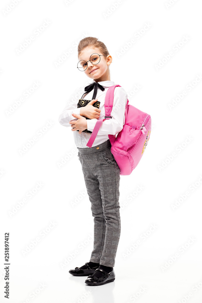 Back to school. Beautiful little girl dressed like a School girl - in white shirt and gray pants, rounded glasses, hold a book with school bag and posing like model. Isolated on white background. Back to school. Beautiful little girl dressed like a School girl - in white shirt and gray pants, rounded glasses, hold a book with school bag and posing like model. Isolated on white background.