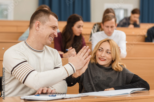 Cheerful man and woman in wheelchair looking at each other and giving five at university. Positive adult students learning new material in lecture hall. Concept of equality and happiness.