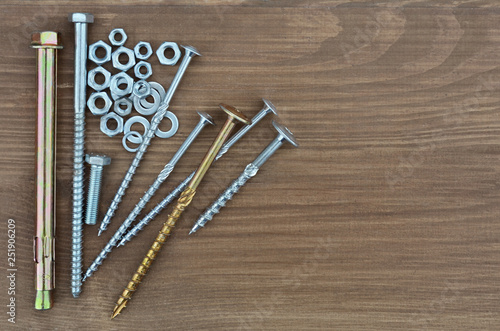 Several various metal fasteners for construction. Self-tapping screw screws, bolt, anker, nuts, washers and washer-grover, close-up on a wooden background.