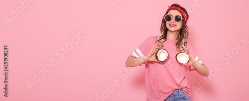 Beautiful young girl in pink t-shirt and glasses holding funny sexy coconuts on pink background