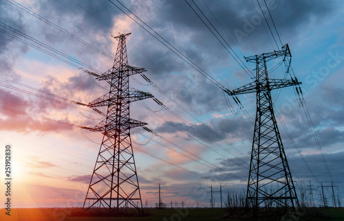 A silhouette of high voltage power lines against a colorful sky at sunrise.