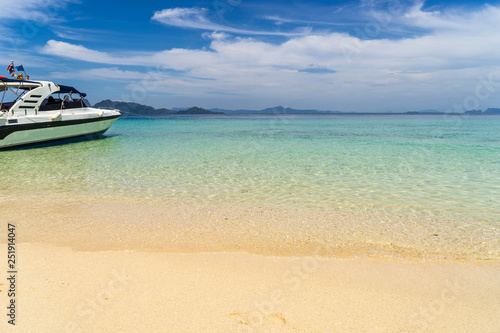Speed boat for tourists anchored on the beach on the island with clear sea water  clean yellow sand  mountains in distance and beautiful sky.