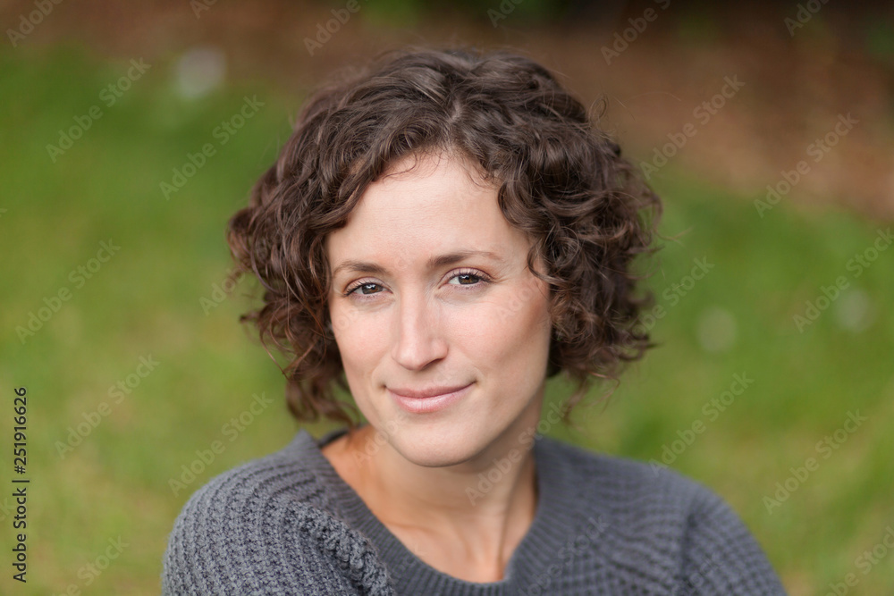 Pretty curly hair woman, relaxing and smiling at the park. She is so calm in peace
