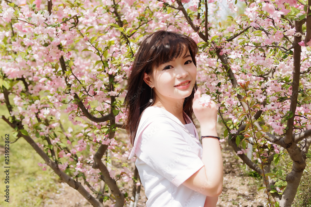 Outdoor portrait of beautiful young Chinese girl smiling among blossom cherry tree brunch in spring garden, beauty, summer, emotion, expression and people lifestyle concept. Outdoor portrait of beautiful young Chinese girl smiling among blossom cherry tree brunch in spring garden, beauty, summer, emotion, expression and people lifestyle concept.