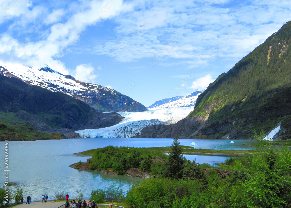 Mendenhall Glacier on a bright sunny day with clear blue skies, waterfall, and green trees