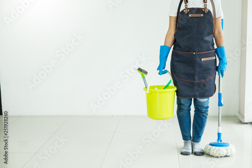 Young housekeeper cleaning floor mobbing holding mop and plastic bucket with brushes  gloves and detergents in the leaving room house floor helping his wife.
