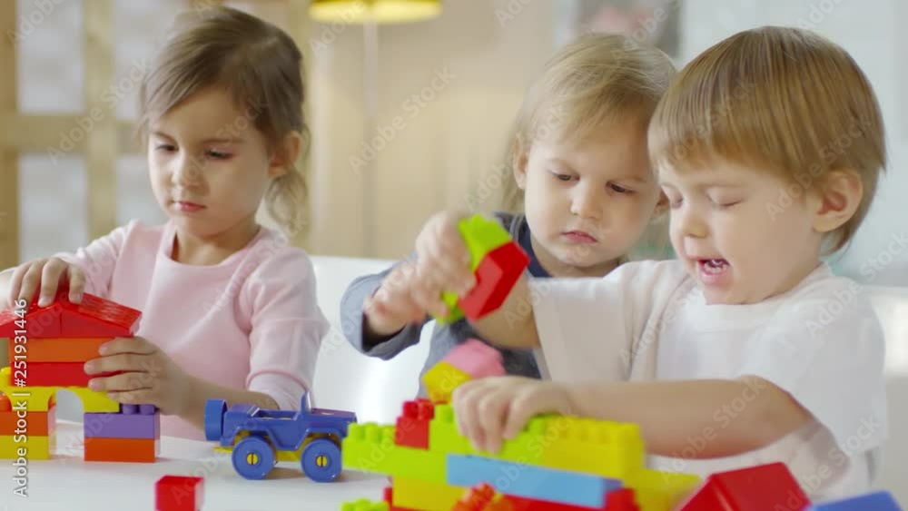 Two little caucasian boys and pretty girl playing with educational construction toys at table in kindergarten Two little caucasian boys and pretty girl playing with educational construction toys at table in kindergarten