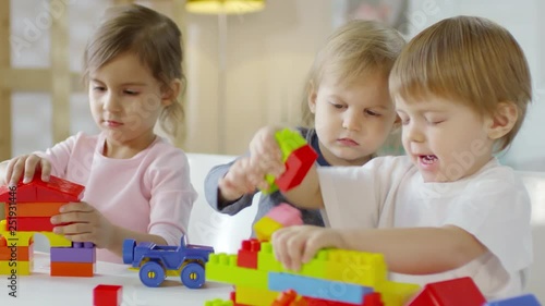 Two little caucasian boys and pretty girl playing with educational construction toys at table in kindergarten photo