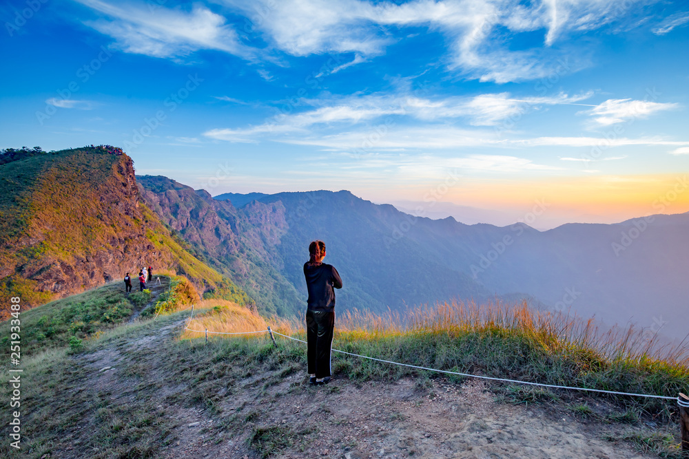 Fototapeta premium Woman waiting for sunrise at Sanknokwua (San Knok Wua) hill at Khao Laem National Park, Kanchanaburi, Thailand. Abstract of freedom and Peaceful with natural clear sky background