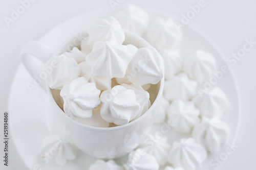 The white merengue in the white tea cup on white background, on white plate, top view