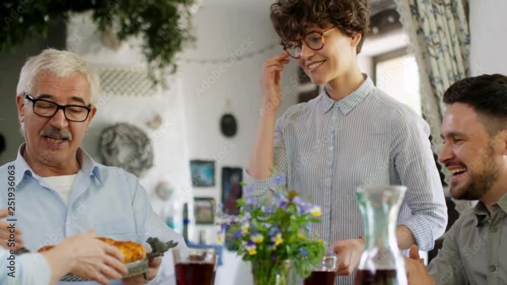 Tracking left of young woman with short curly hair giving pie to her family sitting at dinner table Tracking left of young woman with short curly hair giving pie to her family sitting at dinner table