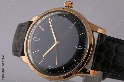 Men's watch with black leather strap,black dial, in golden body,golden clockwise and numerals isolated on gray background.