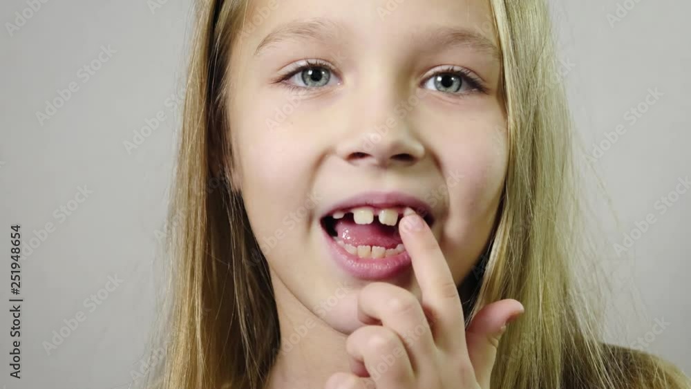 Close - up of cute smiling girl, baby wagging finger milk Fang indoors with white background. Tooth loss by age concept. 4k resolution