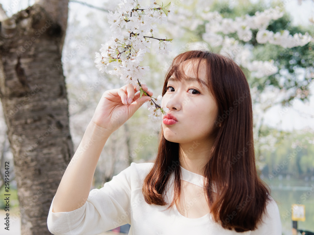 Outdoor portrait of beautiful young Chinese girl smiling among blossom cherry tree brunch in spring garden, beauty, summer, emotion, expression and people lifestyle concept. Outdoor portrait of beautiful young Chinese girl smiling among blossom cherry tree brunch in spring garden, beauty, summer, emotion, expression and people lifestyle concept.