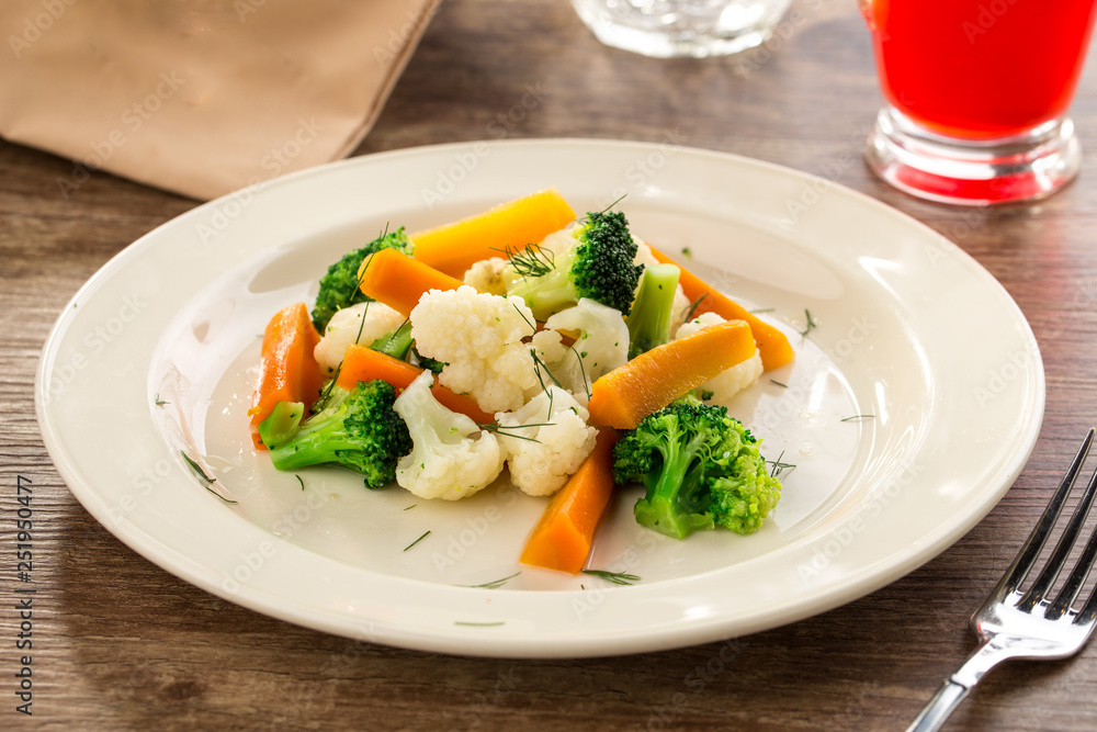 Mixed vegetables cauliflower, broccoli and carrots on white plate on wooden background Mixed vegetables cauliflower, broccoli and carrots on white plate on wooden background
