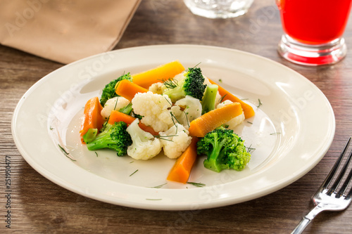 Mixed vegetables cauliflower, broccoli and carrots on white plate on wooden background