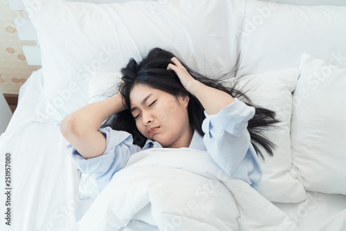 Asian woman yawn and awake up with clock alarm in her bedroom at home. Asian woman lazy wake up to work in morning Monday.