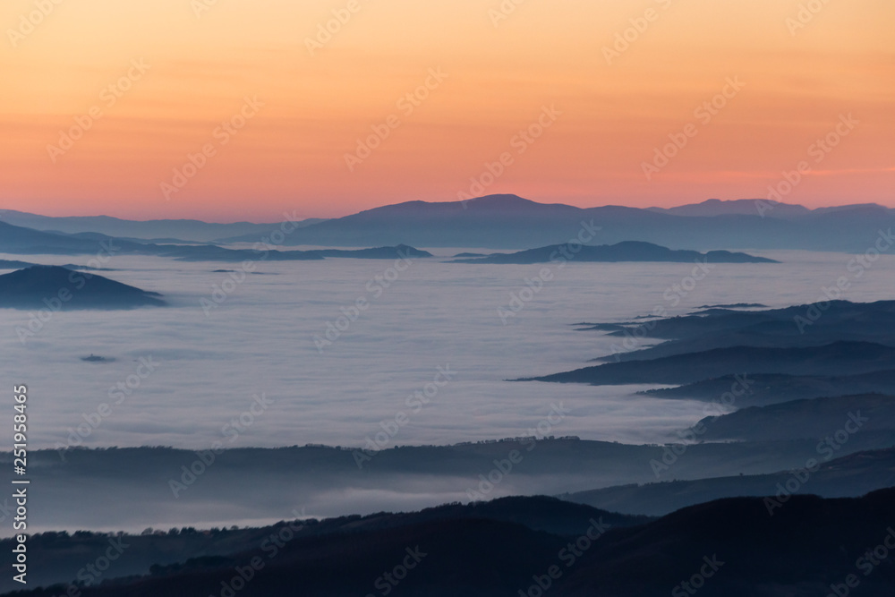 Beautifully colored sky at dusk, with mountains layers over a sea of fog