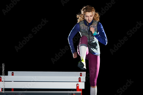 Young female athlete training running with hurdles